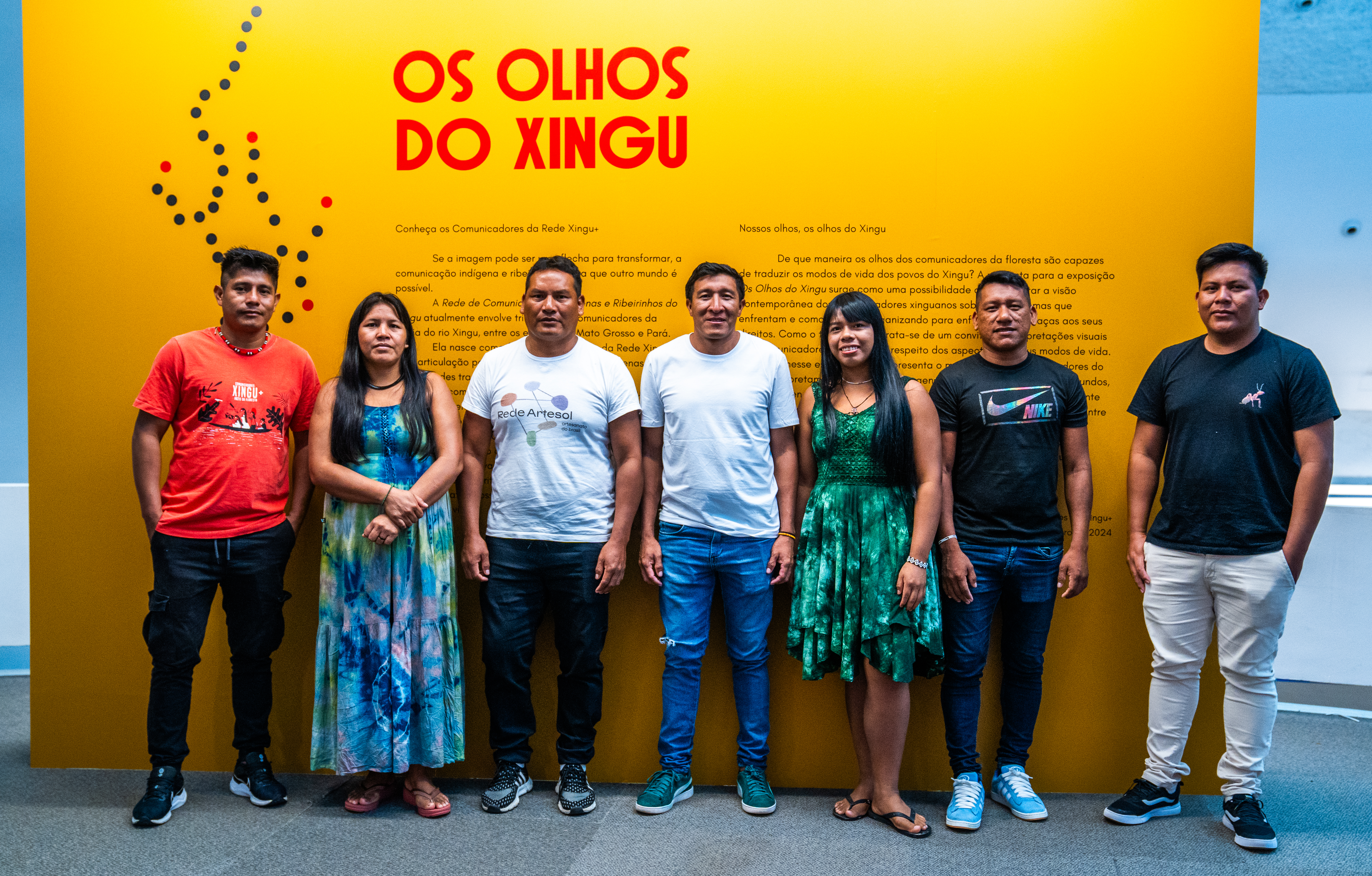 Os fotógrafos expositores posam para foto na frente do cartaz da exposição|Kamikiá Kisêdjê/Rede Xingu+/ISA